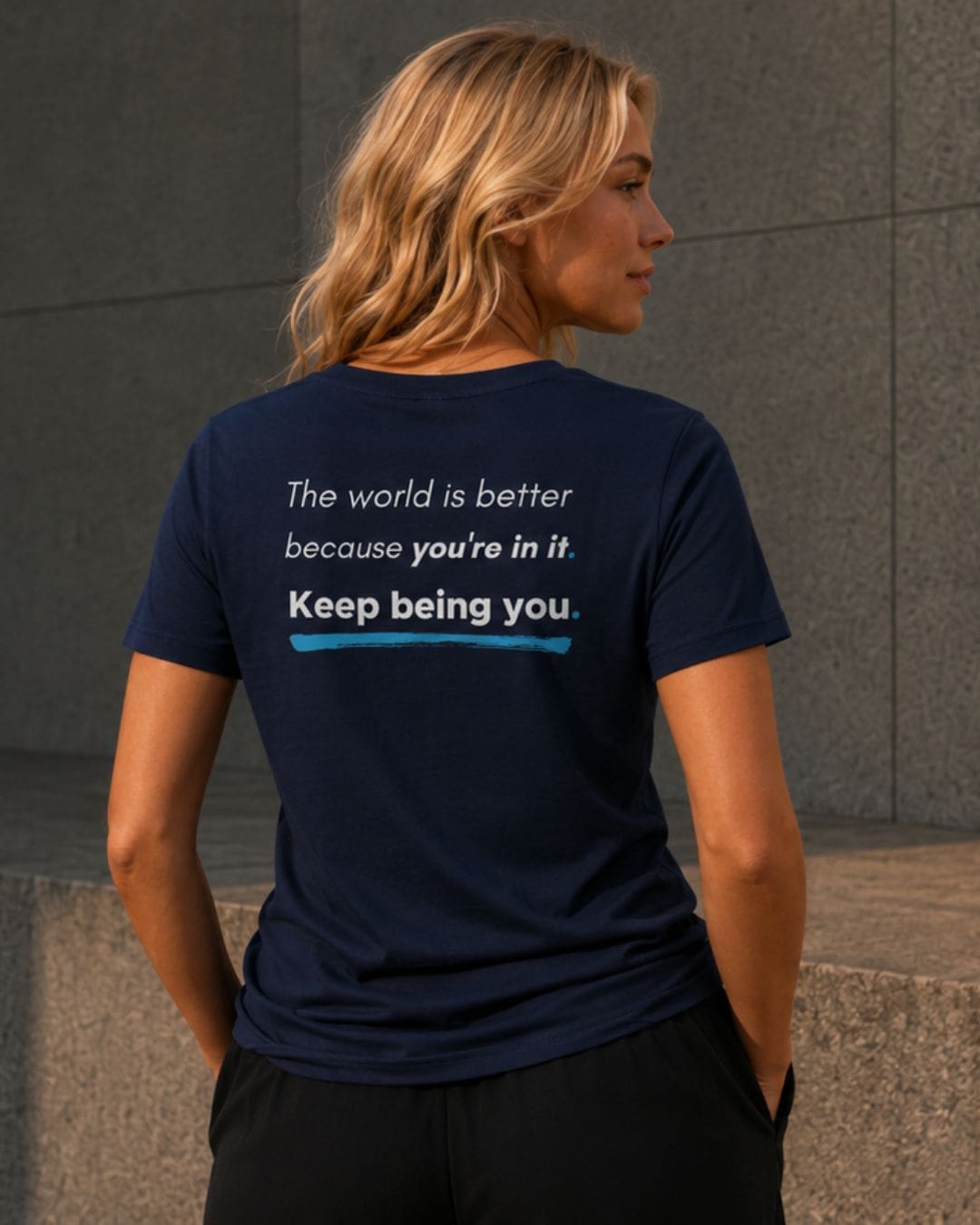 Woman wearing a navy You Are Enough T-shirt with the back message, “The world is better because you’re in it. Keep being you.”